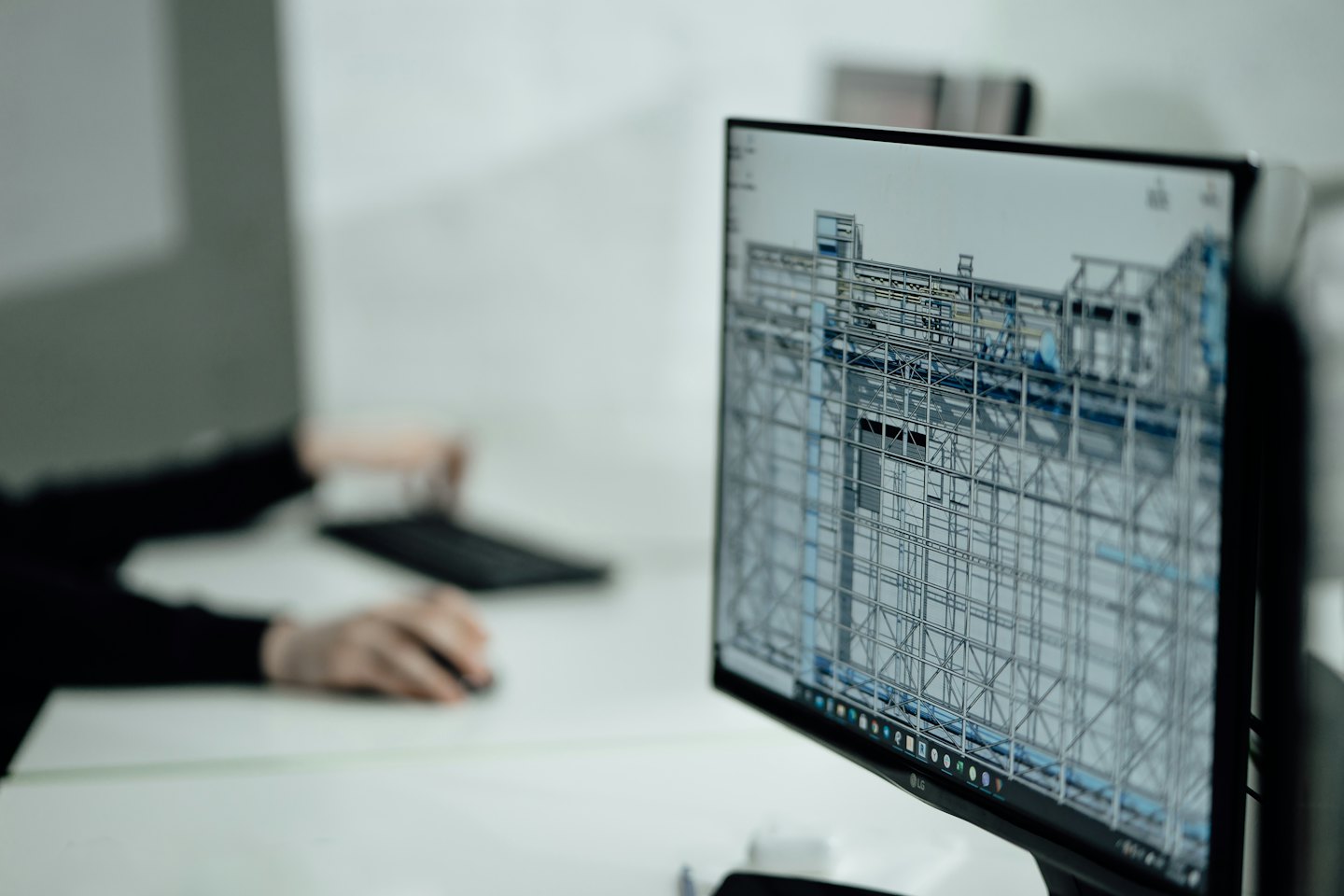 Computer monitor displays 3D wireframe model with hands on keyboard.
